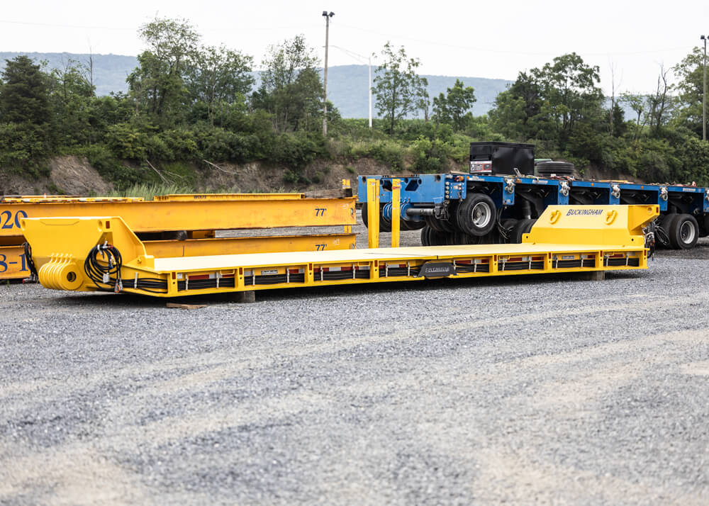 Side view of Goldhofer Heavy Duty Low Profile Deck with trailer and beams in background